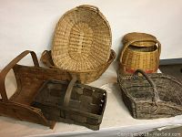 Photo showing two large rectangular laundry type baskets with handles, one round basket with handle and lid, and a dark wooden rectangular basket used as a log holder.