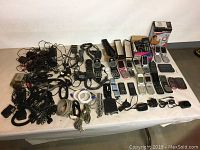 Full view of lot showing all phones laid out along with chargers, cables, and audio accessories on a white surface.