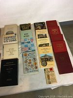 Overview of assorted hardback numismatic books on a table including coin catalogs, counterfeit guides, and investment books.