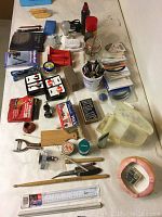 Overview photo showing multiple items on a table including playing cards, pens, tools, rulers, chime boxes, coin tubes and other miscellaneous small household items.