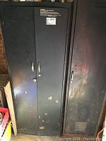 Double-door metal locker with black finish showing paint chips and scratches