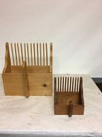 Large and small wooden hand-held cranberry rakes standing side by side on a white surface.