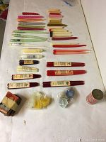 Photo showing assorted tapered candles in colors such as red, green, beige, and yellow laid out flat on a white surface.