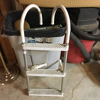 White three-step boat ladder with curved handrails standing on concrete floor indoors