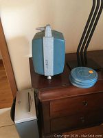 Back/side view of projector on wooden furniture beside two blue film reels.