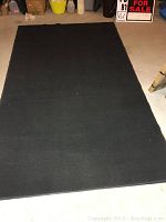 Full view of the black rectangular outdoor rug lying flat on a floor.