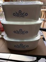 Three rectangular CorningWare casserole dishes stacked with clear glass lids, showing blue cornflower pattern.