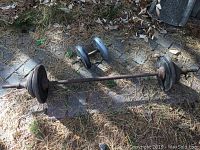 Barbell laid on ground with black weight plates and rusty bar, surrounded by leaves and pine needles