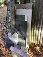 Multiple granite countertop pieces leaning against wooden wall and fence, variety of colors and sizes visible.