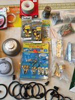 Photo showing various household hardware items and accessories including picture hangers, hooks, hinges, wire coil, and fasteners laid out on a work surface with measuring tape at top edge.