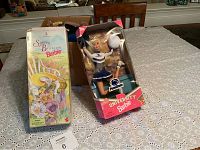 Spring Blossom Barbie in original box with noticeable wear and Penn State University Barbie in cheerleader outfit in original box on table.