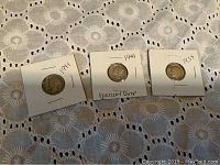 Three dimes mounted individually in white cardboard coin holders labeled 1941, 1944 Mercury Dime, and 1954 Roosevelt Dime on a white floral patterned surface.