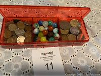 Red plastic container with three compartments holding marbles, coins, and tokens on a white textured cloth