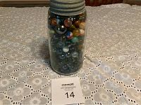 Full view of the jar showing the top and marbles inside on a lace tablecloth.