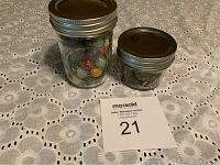 Two glass jars displayed on a lace tablecloth, one jar contains pennies and the other contains marbles.