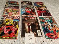 Photo showing 15 Marvel comic books in plastic sleeves arranged on table, featuring titles like Avengers West Coast, Daredevil, Defenders, and Glorian.