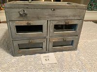 Front view of small free standing cabinet showing four glass front drawers with metal knob handles and glass top lid.