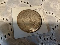 Close-up of the 1879 Morgan silver dollar coin face in protective cardboard holder with '1879' marking