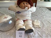 Full view of the astronaut doll seated upright with astronaut helmet helmet and gloves placed next to doll, showing outfit details on table.