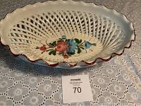 Oval ceramic basket with lattice woven pattern and floral hand-painting inside, resting on lace tablecloth.