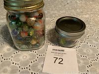 Two jars filled with assorted colorful glass marbles on a white lace tablecloth.