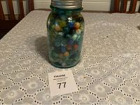 Full jar of various marbles on a table with white lace tablecloth, showing the fill level and types of marbles inside.