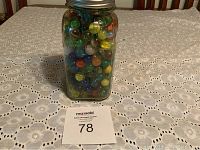 Glass jar filled with various colorful marbles on a lace tablecloth, showing height and lid.