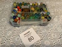 Plastic compartment organizer containing marbles, old coins, and miscellaneous items arranged and labeled by decade.