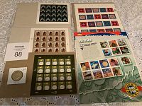 Photo showing a 1967 silver half dollar coin and six sheets of USPS stamps with various thematic designs laid out on a table.