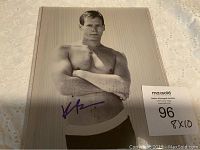 Frontal view of the signed black and white 8x10 photo of Kevin Bacon with auction lot number visible on the plastic sleeve.