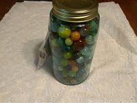 Front view of jar filled with marbles showing attached plastic bag with stamps