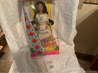 Front view of never used Native American Barbie doll in original packaging, showing doll with black hair in traditional inspired white dress with bead patterns, along with colorful beaded sash.