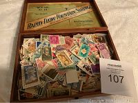 Top-down view of vintage wooden cigar box filled with assorted stamps, showing the box interior label and a variety of stamps.