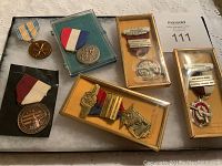 Overall view of eight medals with ribbons and in display boxes on a white tablecloth.