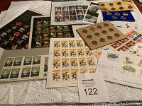Wide view of assortment of vintage postage stamp sheets, penny coin sets, and quarter coin set on lace tablecloth.