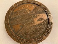 Close-up photo of large bronze medal showing raised image of the Delaware Water Gap Bridge and surrounding landscape with inscription.