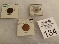 Three coins labeled and mounted in holders: 1964 chipped planchet penny, blank planchet error coin, mini Indian Head cent 1897, with auction lot number visible.