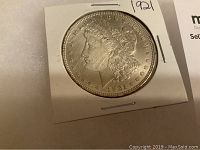 Obverse of 1921 Morgan Silver Dollar coin showing Lady Liberty profile in cardboard holder.