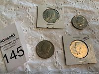 Four half dollar coins including 1964 90% silver, 1967 40% silver, and two 1971 half dollars arranged on a fabric surface.