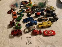 Photo showing an overview of toy cars and figurines arranged on a white cloth with auction lot tag visible.
