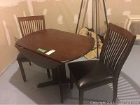 Photo of dining table with both leaves down and two matching chairs placed around it in a basement environment showing the overall condition and design.