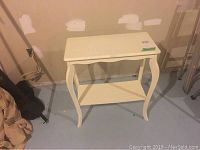 White wooden table with refinished surface, curved legs, and lower shelf placed against basement wall.