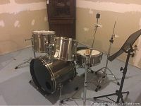 Full drum kit setup showing bass drum, mounted rack toms, floor tom, snare on stand, cowbell on stand, drum throne and music stand