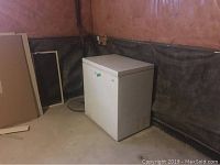 Kenmore white chest freezer with top-opening lid, showing wear, placed in basement corner