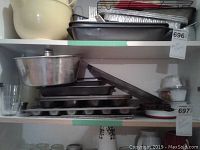 Shelf with stacked metal baking pans including muffin and square pans, metal cooling rack, and a large metal mixing bowl.
