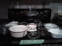 White Corningware casserole dishes with blue cornflower pattern, multiple clear glass bowls and bakeware on stove top.