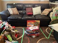 Front view of the dark brown leather sofa with five throw pillows arranged along the backrest. Various toys and board games are visible in the foreground.