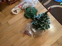 Green ceramic Christmas tree partially disassembled showing base with light bulb as well as bag of extra plastic lights.