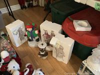 Photo showing multiple snowman figurines out of their original styrofoam packaging on hardwood floor, including a snowman with a scarf, dancing snowman, and ceramic top hat candle holder.