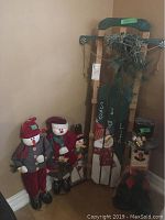 Full view of all five decorations arranged in corner showing two stuffed snowmen, two wooden snowman block figures, and wooden sled decorated with pine branches.